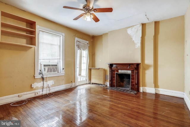 unfurnished living room with dark wood-type flooring, a brick fireplace, ceiling fan, and radiator heating unit