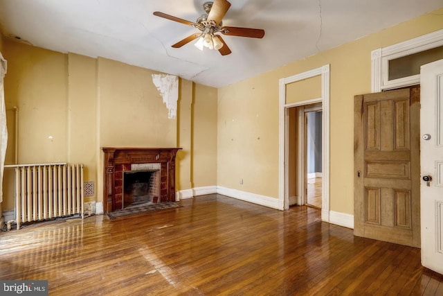 unfurnished living room with dark hardwood / wood-style flooring, ceiling fan, radiator, and a fireplace