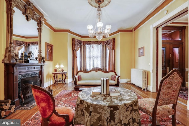 sitting room with light wood-type flooring, crown molding, a chandelier, and radiator heating unit