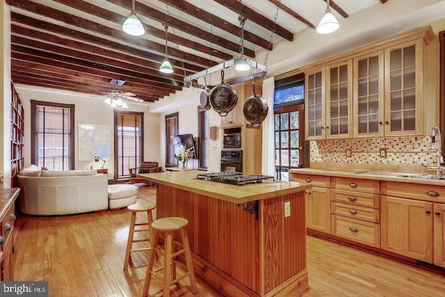 kitchen featuring ceiling fan, a kitchen island, beamed ceiling, a breakfast bar area, and tasteful backsplash