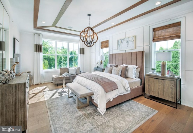 bedroom with a notable chandelier, light wood-type flooring, and a tray ceiling