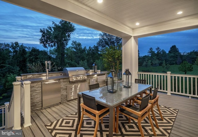 deck at dusk featuring a grill and an outdoor kitchen