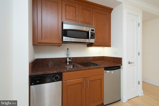 kitchen with appliances with stainless steel finishes, dark stone countertops, and light hardwood / wood-style floors