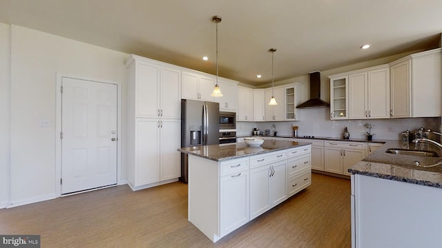 kitchen featuring pendant lighting, a kitchen island, wall chimney range hood, light hardwood / wood-style flooring, and appliances with stainless steel finishes