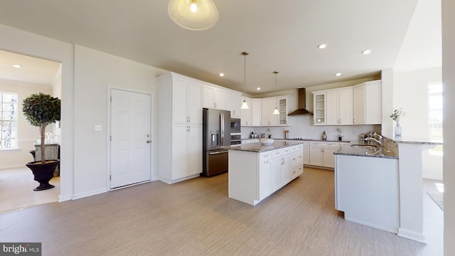 kitchen with pendant lighting, dark stone counters, appliances with stainless steel finishes, white cabinets, and wall chimney range hood