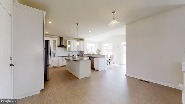 kitchen featuring decorative light fixtures, white cabinetry, a kitchen island, wall chimney exhaust hood, and stainless steel refrigerator