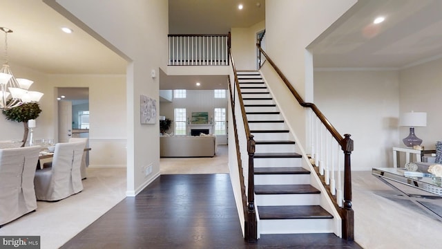 stairs featuring crown molding, dark wood-type flooring, a chandelier, and a high ceiling