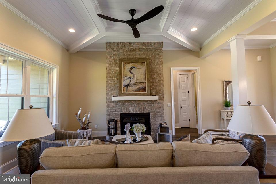 living room with wood-type flooring, ceiling fan, decorative columns, a brick fireplace, and ornamental molding