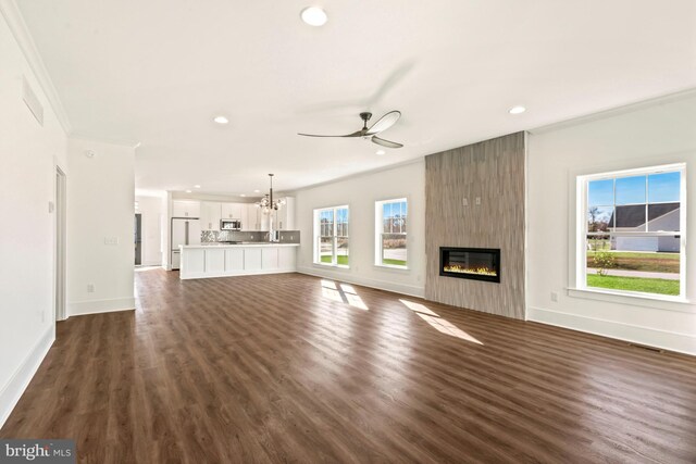 unfurnished living room featuring dark wood-type flooring, ceiling fan with notable chandelier, a large fireplace, and plenty of natural light