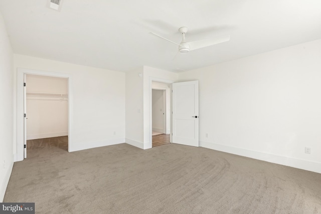 unfurnished bedroom featuring light carpet, a walk in closet, and ceiling fan