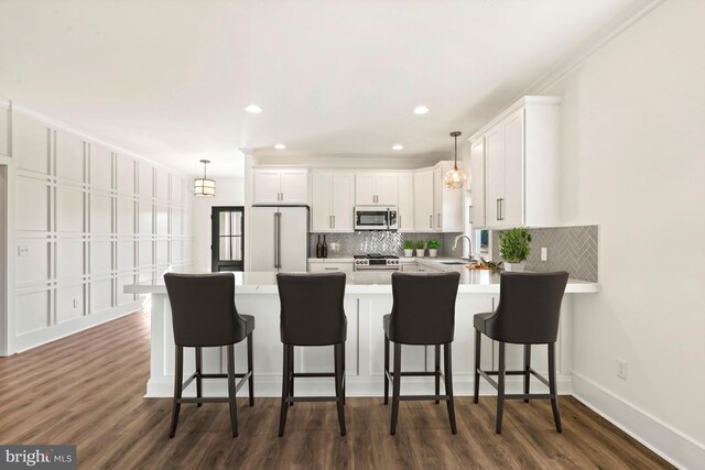 kitchen with kitchen peninsula, white cabinetry, appliances with stainless steel finishes, dark hardwood / wood-style flooring, and a breakfast bar area