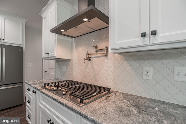 kitchen featuring appliances with stainless steel finishes, light stone counters, white cabinetry, and wall chimney exhaust hood