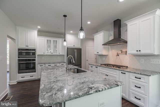 kitchen with hanging light fixtures, stainless steel appliances, wall chimney exhaust hood, and white cabinets