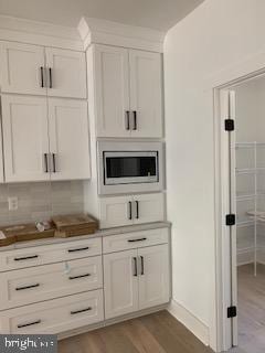 kitchen with light wood-type flooring, tasteful backsplash, stainless steel microwave, and white cabinetry