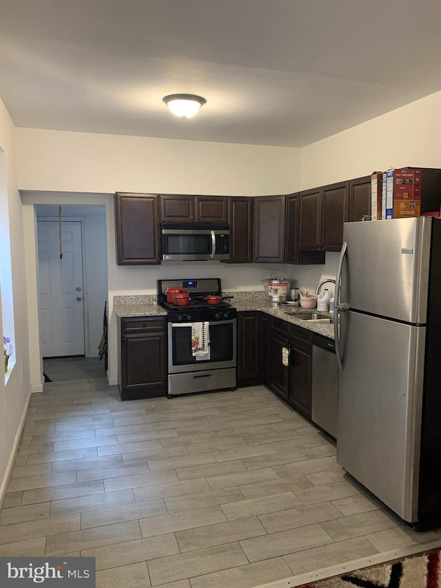 kitchen featuring sink, light stone counters, dark brown cabinets, stainless steel appliances, and light wood-type flooring