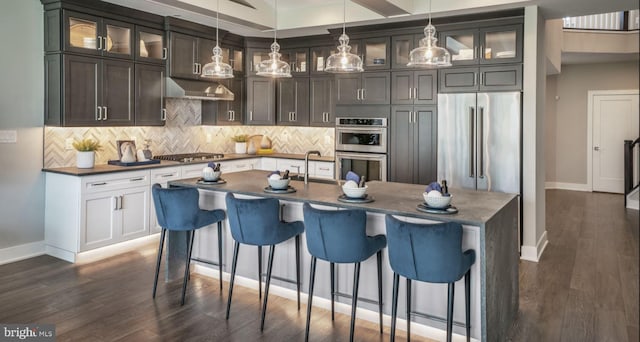 kitchen with backsplash, a kitchen island with sink, stainless steel appliances, dark hardwood / wood-style flooring, and a breakfast bar area