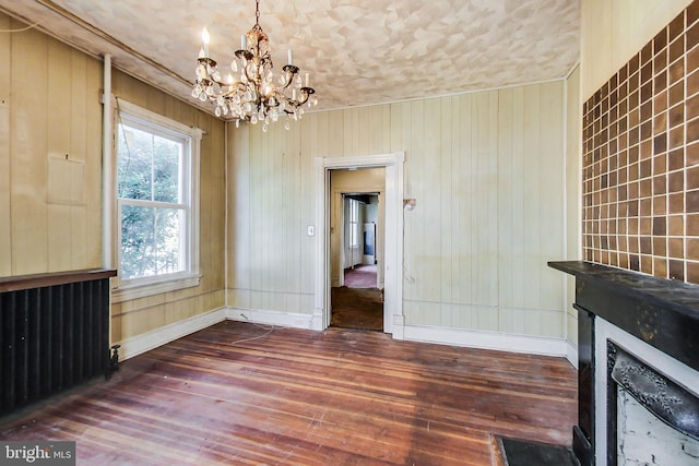 unfurnished living room featuring an inviting chandelier, dark hardwood / wood-style floors, and radiator