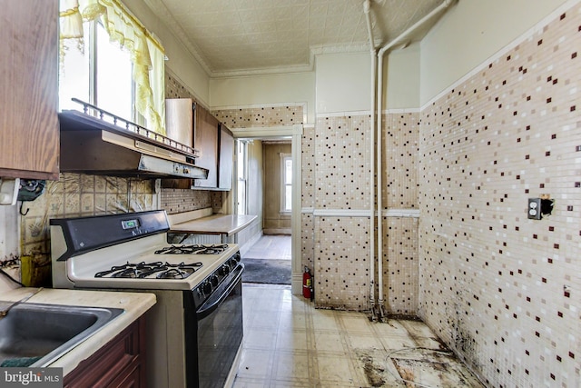 kitchen with tasteful backsplash, crown molding, white gas range, sink, and light tile flooring