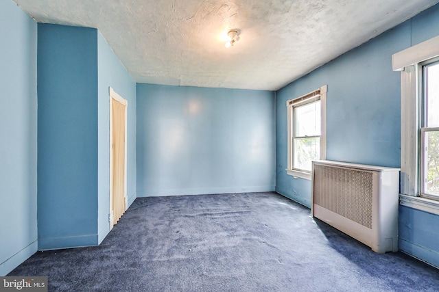 carpeted empty room with a textured ceiling, a wealth of natural light, and radiator