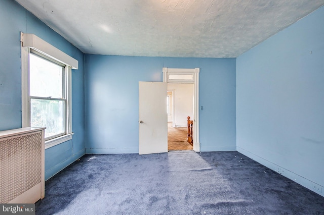 spare room featuring radiator heating unit, dark colored carpet, and a textured ceiling