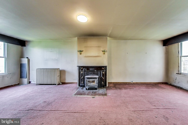 unfurnished living room with carpet flooring, a wood stove, radiator heating unit, and a wealth of natural light