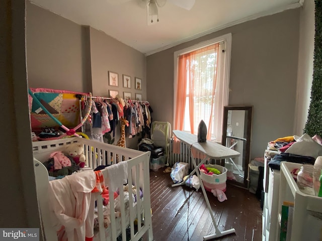 bedroom featuring ceiling fan, dark hardwood / wood-style floors, and a nursery area