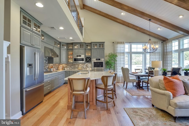 kitchen with pendant lighting, stainless steel appliances, a notable chandelier, wall chimney range hood, and a kitchen island with sink