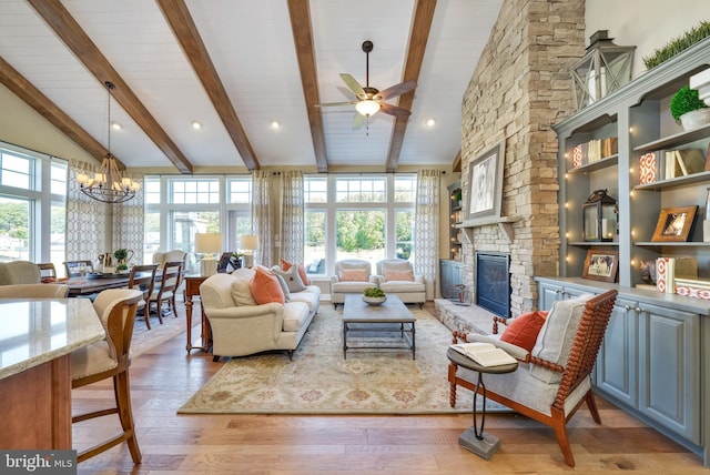 living room featuring light hardwood / wood-style flooring, a stone fireplace, beamed ceiling, and ceiling fan with notable chandelier