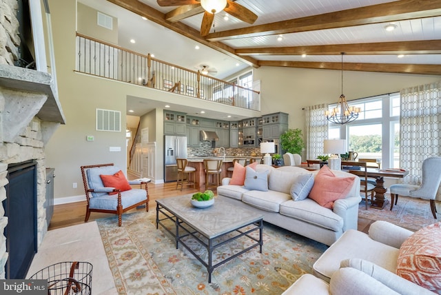 living room with a fireplace, ceiling fan with notable chandelier, beam ceiling, and high vaulted ceiling