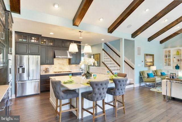 kitchen with hanging light fixtures, wall chimney range hood, a center island, dark wood-type flooring, and stainless steel fridge