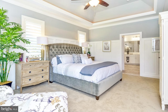 bedroom featuring ceiling fan, light colored carpet, ensuite bathroom, and a tray ceiling