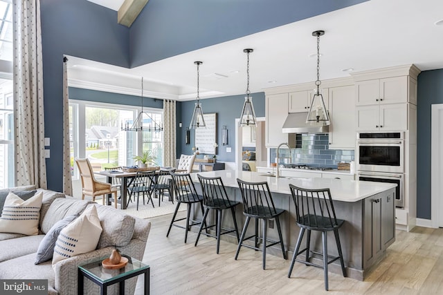 kitchen with white cabinetry, appliances with stainless steel finishes, a breakfast bar, light wood-type flooring, and a center island with sink