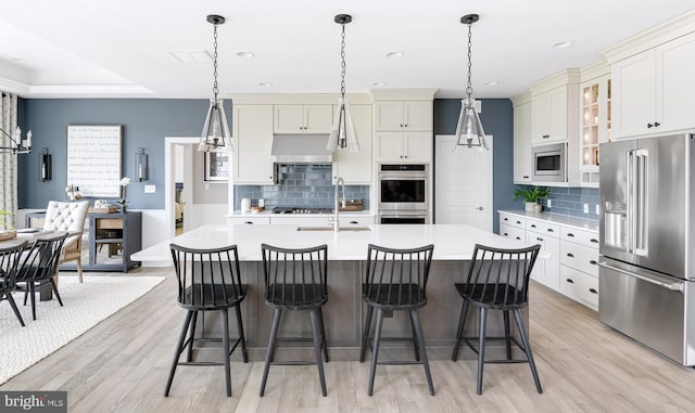 kitchen with appliances with stainless steel finishes, a kitchen bar, light wood-type flooring, a kitchen island with sink, and hanging light fixtures