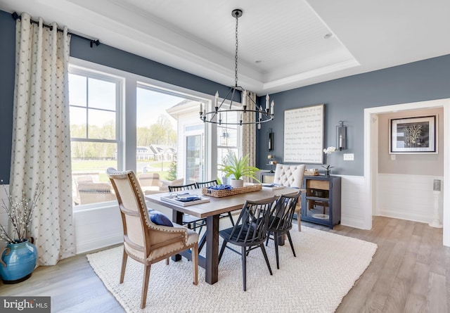 dining space with a raised ceiling, an inviting chandelier, and light wood-type flooring