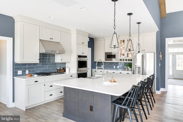 kitchen featuring stainless steel appliances, light wood-type flooring, and a kitchen island with sink