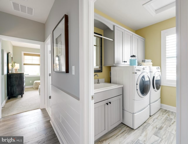 laundry area with separate washer and dryer, light hardwood / wood-style flooring, cabinets, and a healthy amount of sunlight