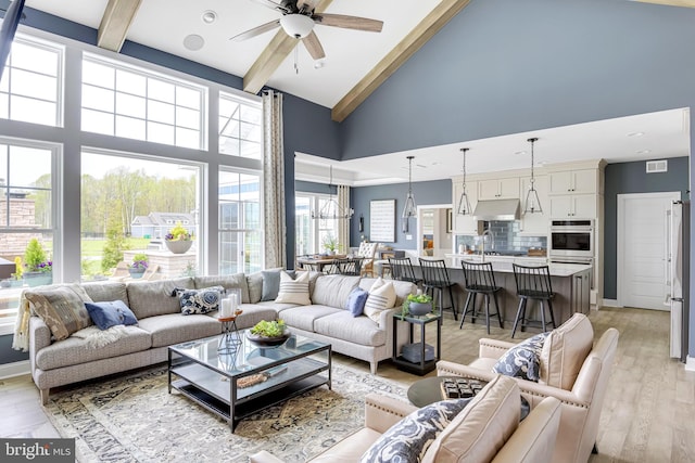 living room with a high ceiling, beam ceiling, ceiling fan, and light wood-type flooring