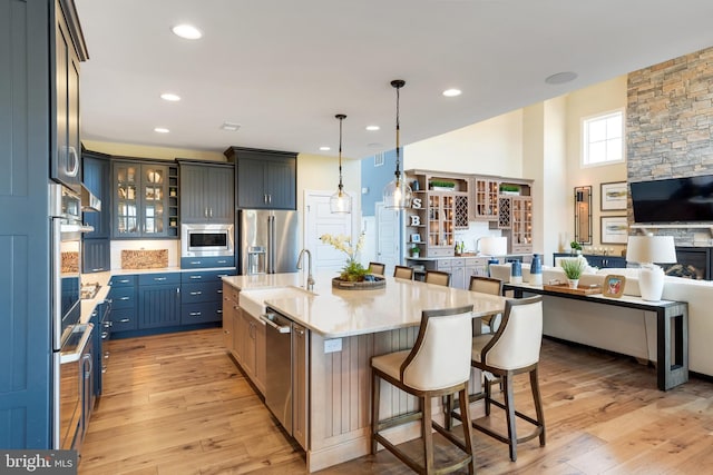 kitchen featuring hanging light fixtures, a fireplace, appliances with stainless steel finishes, light hardwood / wood-style flooring, and a center island with sink