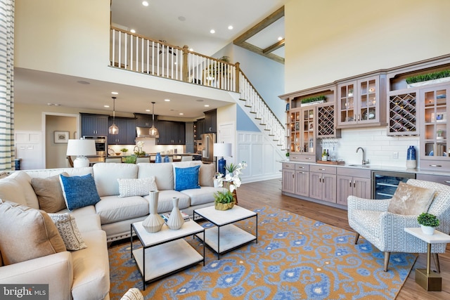 living room featuring sink, beverage cooler, hardwood / wood-style floors, and a towering ceiling