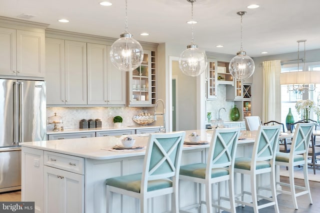 kitchen featuring a kitchen island with sink, a breakfast bar, light hardwood / wood-style floors, high quality fridge, and tasteful backsplash