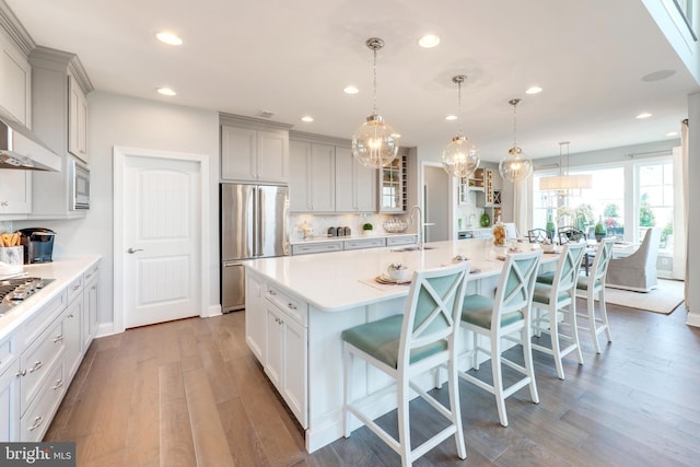 kitchen with hardwood / wood-style flooring, appliances with stainless steel finishes, an island with sink, and a kitchen breakfast bar