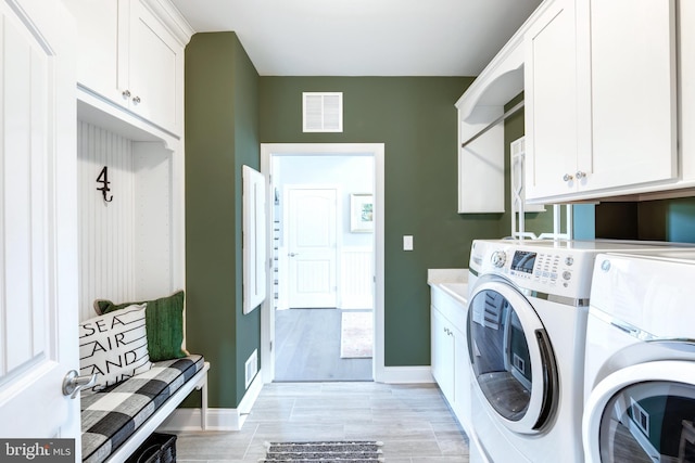 washroom featuring independent washer and dryer, cabinets, and light hardwood / wood-style floors