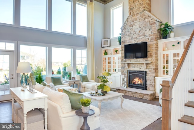 living room with a high ceiling, a stone fireplace, and wood-type flooring