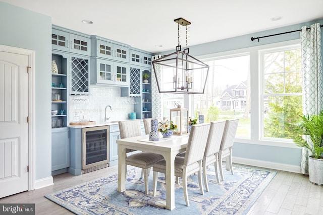 dining area with a chandelier, wine cooler, light wood-type flooring, and sink