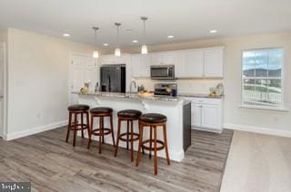 kitchen featuring fridge, light hardwood / wood-style floors, white cabinetry, a kitchen bar, and pendant lighting