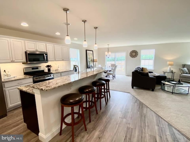 kitchen featuring pendant lighting, a notable chandelier, appliances with stainless steel finishes, white cabinets, and light wood-type flooring