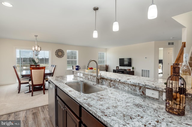 kitchen with pendant lighting, a notable chandelier, sink, light stone countertops, and light carpet