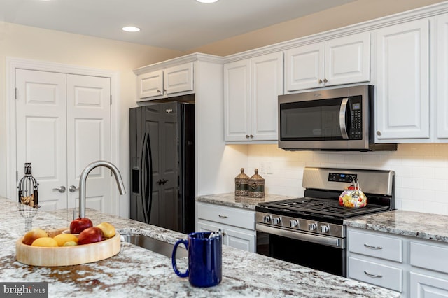 kitchen with appliances with stainless steel finishes, light stone countertops, backsplash, and white cabinetry