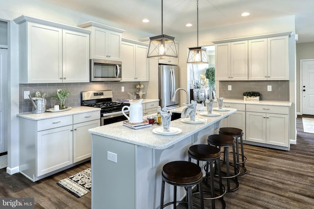 kitchen featuring dark hardwood / wood-style flooring, decorative light fixtures, appliances with stainless steel finishes, and an island with sink