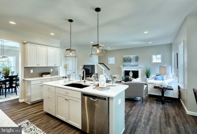 kitchen featuring dark wood-type flooring, white cabinetry, stainless steel dishwasher, an island with sink, and sink